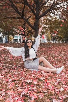 a woman sitting on the ground with her arms outstretched in front of trees and leaves