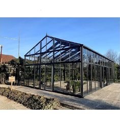 a greenhouse with glass walls and plants in the ground next to it on a sunny day