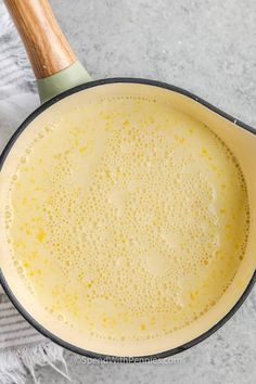 a pan filled with yellow liquid on top of a white countertop next to a wooden spoon