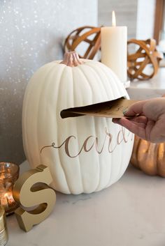 a white pumpkin sitting on top of a table next to a hand holding a candle