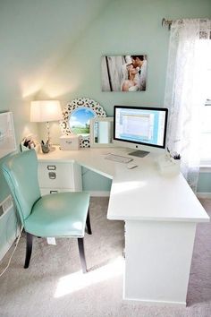 a white desk topped with a computer monitor next to a blue chair and windowsill