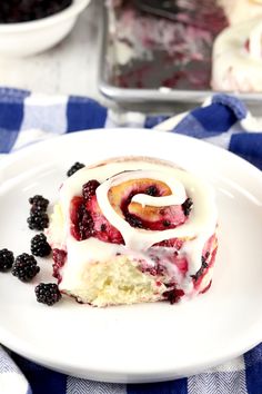 a white plate topped with a piece of cake covered in icing and blackberries