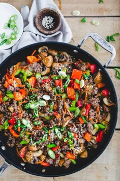 a skillet filled with meat and vegetables on top of a wooden table