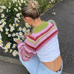 a woman sitting on the ground in front of some daisies looking at her cell phone