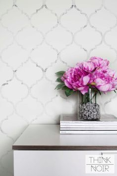 a vase with pink flowers sitting on top of a dresser next to a white wall