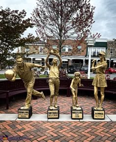 three bronze statues of people playing basketball in front of a bench on a brick walkway