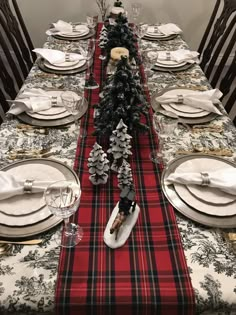 the table is set for christmas dinner with white plates and silverware, black and red plaid runner