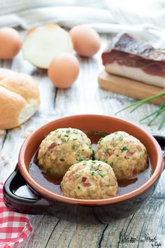 three meatballs are in a bowl on a table with bread and other food items