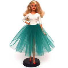 a barbie doll wearing a green tulle skirt and white shirt with red shoes on