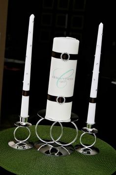 three white candles sitting on top of a green place mat with silver rings around them