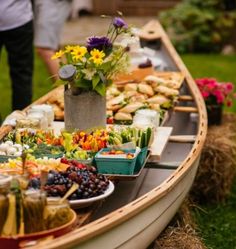 a long boat filled with lots of food on top of a grass covered field next to people