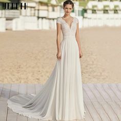 a woman in a white wedding dress standing on a wooden deck at the beach with her back to the camera