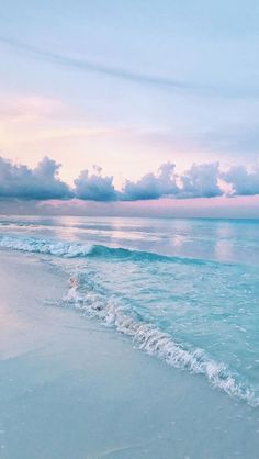 an ocean beach with waves coming in to the shore and clouds over the water at sunset