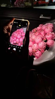 a person taking a photo with their cell phone of pink roses in a bouquet on display