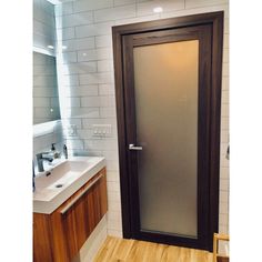 a bathroom with a wooden floor and white tiled walls, has a glass door to the outside