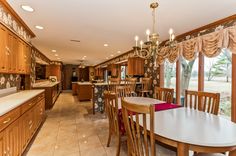 a dining room and kitchen area with wood cabinets, tile flooring and large windows