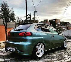 the rear end of a green car parked on a cobblestone street