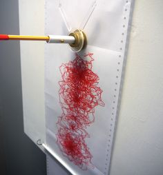 a piece of paper with red thread on it being held up by a needle and pinned to the wall