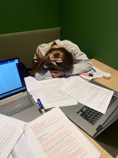 a girl is sleeping on her desk with many papers and laptops in front of her