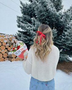 a woman standing in front of a pile of logs with a red bow on her head