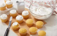 cupcakes with white frosting next to a bowl of icing and a knife