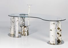 a glass and metal table with two candles on each side, surrounded by white birch trees