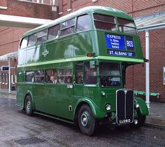 a green double decker bus parked in front of a brick building