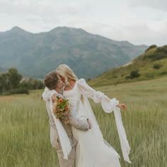 a bride and groom kissing in a field with mountains in the background