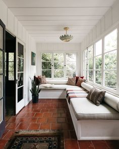 an instagram photo of a sun room with white walls and brick flooring on the bottom level