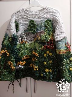 a sweater hanging on a hook in front of a white wall with flowers and trees