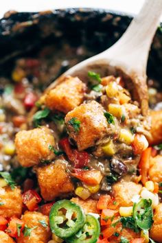 a wooden spoon is full of food that includes tater tots, peppers and corn