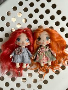 two dolls sitting next to each other on top of a metal grate with holes in it