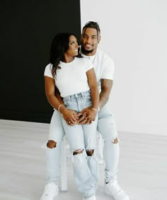 a man and woman sitting on top of a white chair with their arms around each other