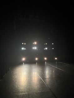 three cars driving down a dark road at night with headlights on and fog in the air