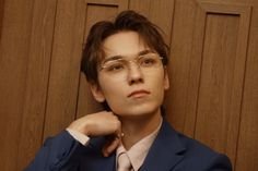 a young man wearing glasses and a suit posing for the camera with his hand on his chin