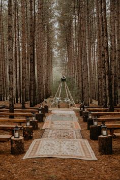 an outdoor ceremony setup in the woods with rows of benches and rugs on the ground