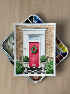 a card with a red door and potted plants in front of it on top of a wooden table