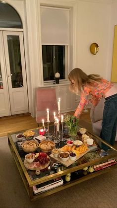 a woman bending over to look at food on a table that has candles in it