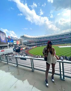 a woman standing in front of a fence at a baseball stadium with the sky above her