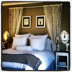 a bed with white sheets and pillows in a bedroom next to two framed pictures on the wall