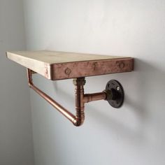 a wooden shelf mounted to the side of a wall with copper pipe fittings on it