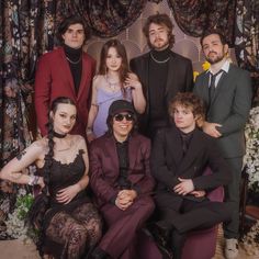 a group of people sitting next to each other in front of a floral wallpaper