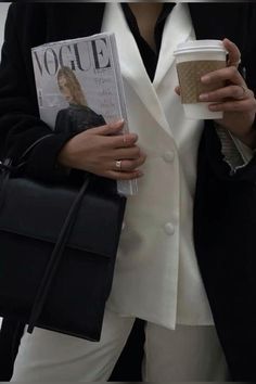 a woman holding a coffee cup and a magazine in her hand while wearing a white blazer