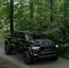 the black truck is driving down the road in front of some green trees and bushes