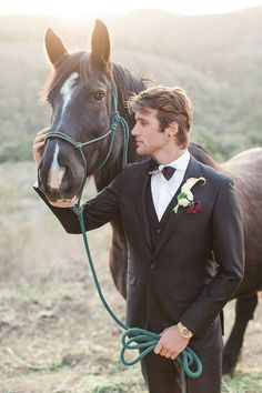 a man in a tuxedo holds the bridle of a brown horse