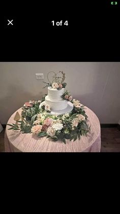 a white wedding cake sitting on top of a table covered in flowers and greenery