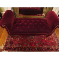 a red couch sitting in front of a mirror on top of a wooden floor next to a rug