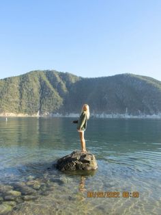 a woman standing on top of a rock in the middle of a body of water