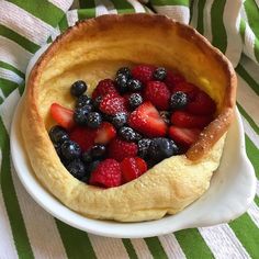 a bowl filled with fruit on top of a green and white striped table cloth next to a fork