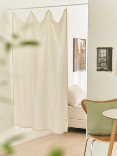 a room with a table, chair and curtains hanging from the ceiling in front of a bed